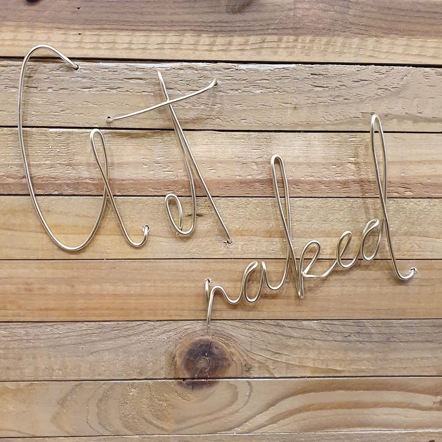 Gold Get Naked Wire Words Wall Art Decoration on a Wood Panel Wall